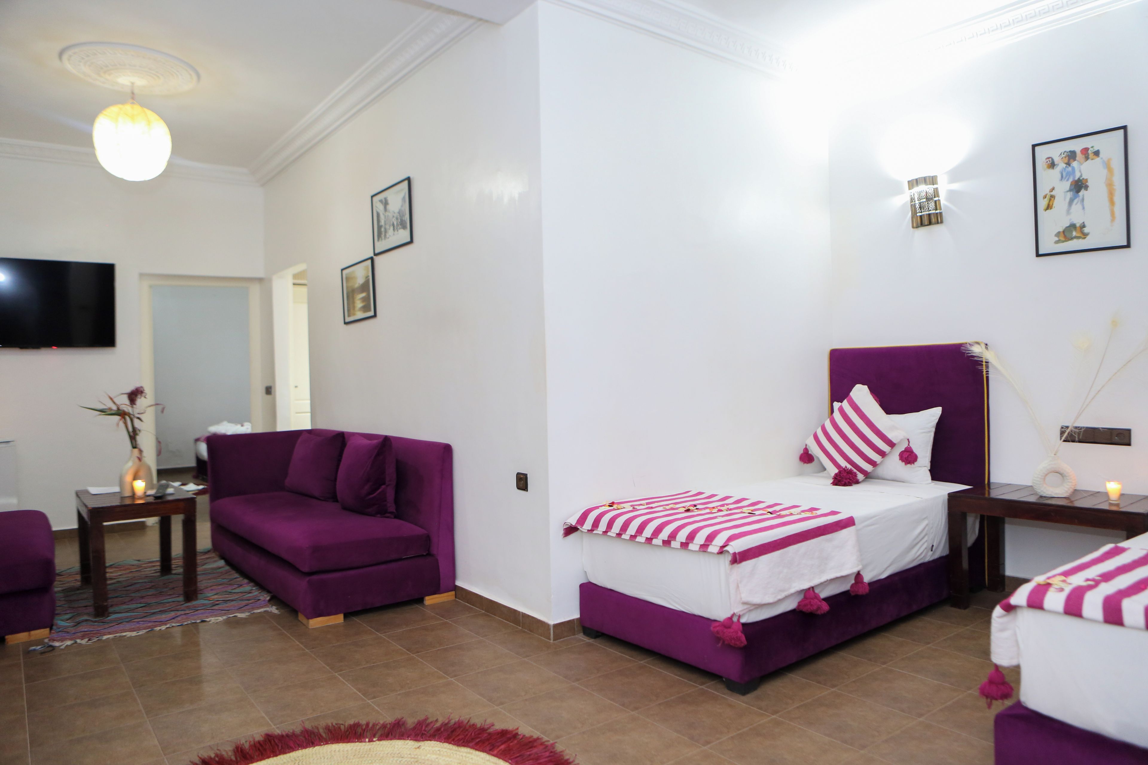 A bedroom with a bed, a sofa, a TV, and a small table with a vase.