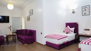 A bedroom with a bed, a sofa, a TV, and a small table with a vase.