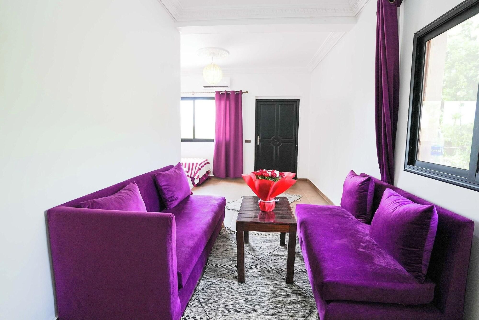 A room with purple sofas, a wooden table, and a window with curtains.