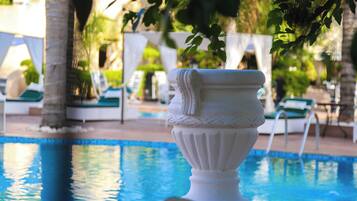 A pool area with a white decorative urn, lounge chairs, and palm trees.