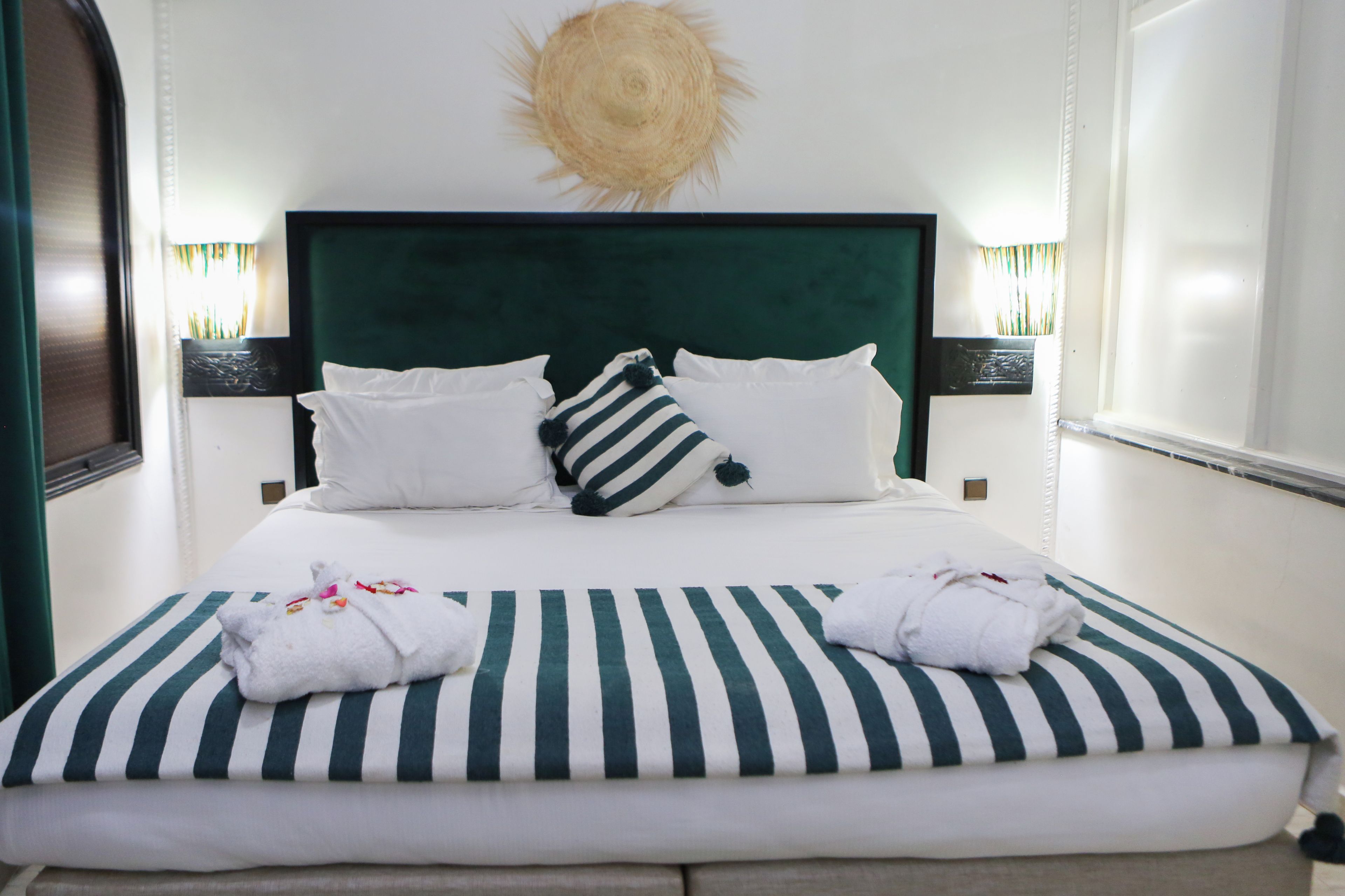 Un letto rifatto con cura, con lenzuola a righe, cuscini bianchi e un decoro a forma di sole sulla parete.