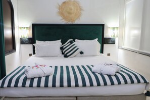 A neatly made bed with striped bedding, white pillows, and a sun-shaped wall decoration. - Weedan Ferme D'hôtes (Marrakech)