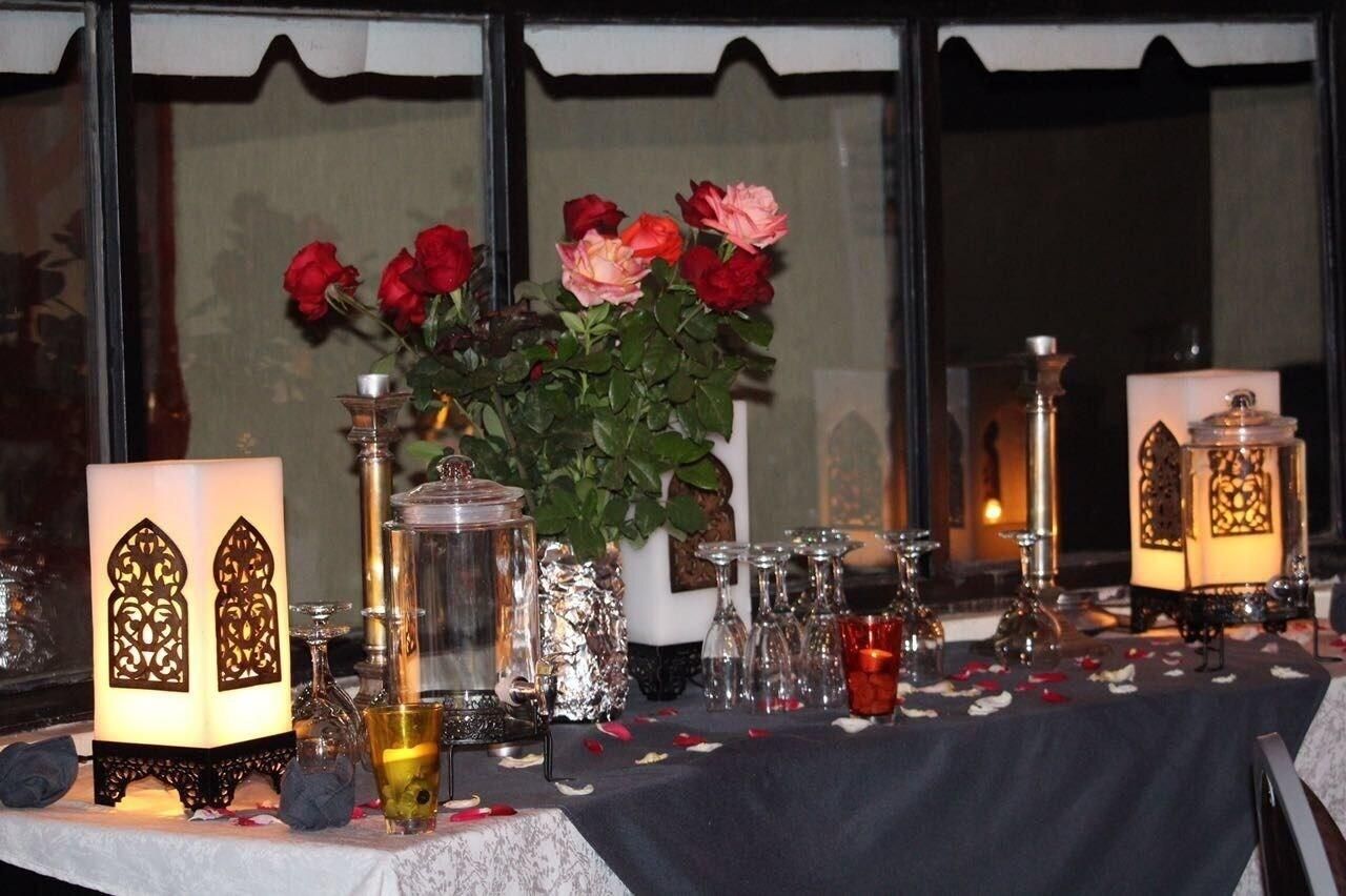 A table set with candles, a vase of roses, and a decorative lantern.