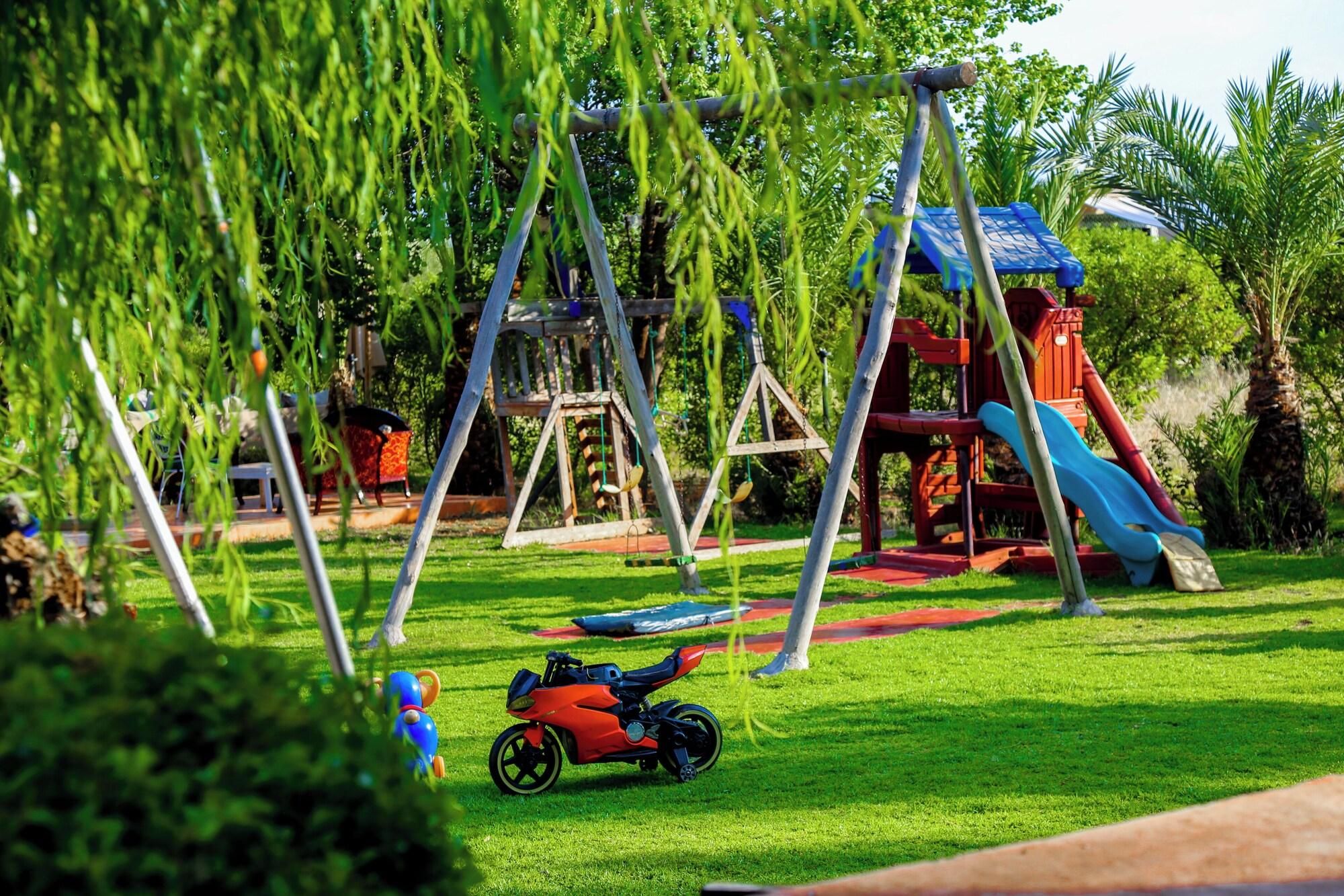 Un parque infantil con columpios, toboganes y un pequeño coche de juguete rojo sobre el césped.