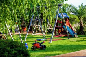 A playground with swings, slides, and a small red toy car on the grass. - Weedan Ferme D'hôtes (Marrakech)