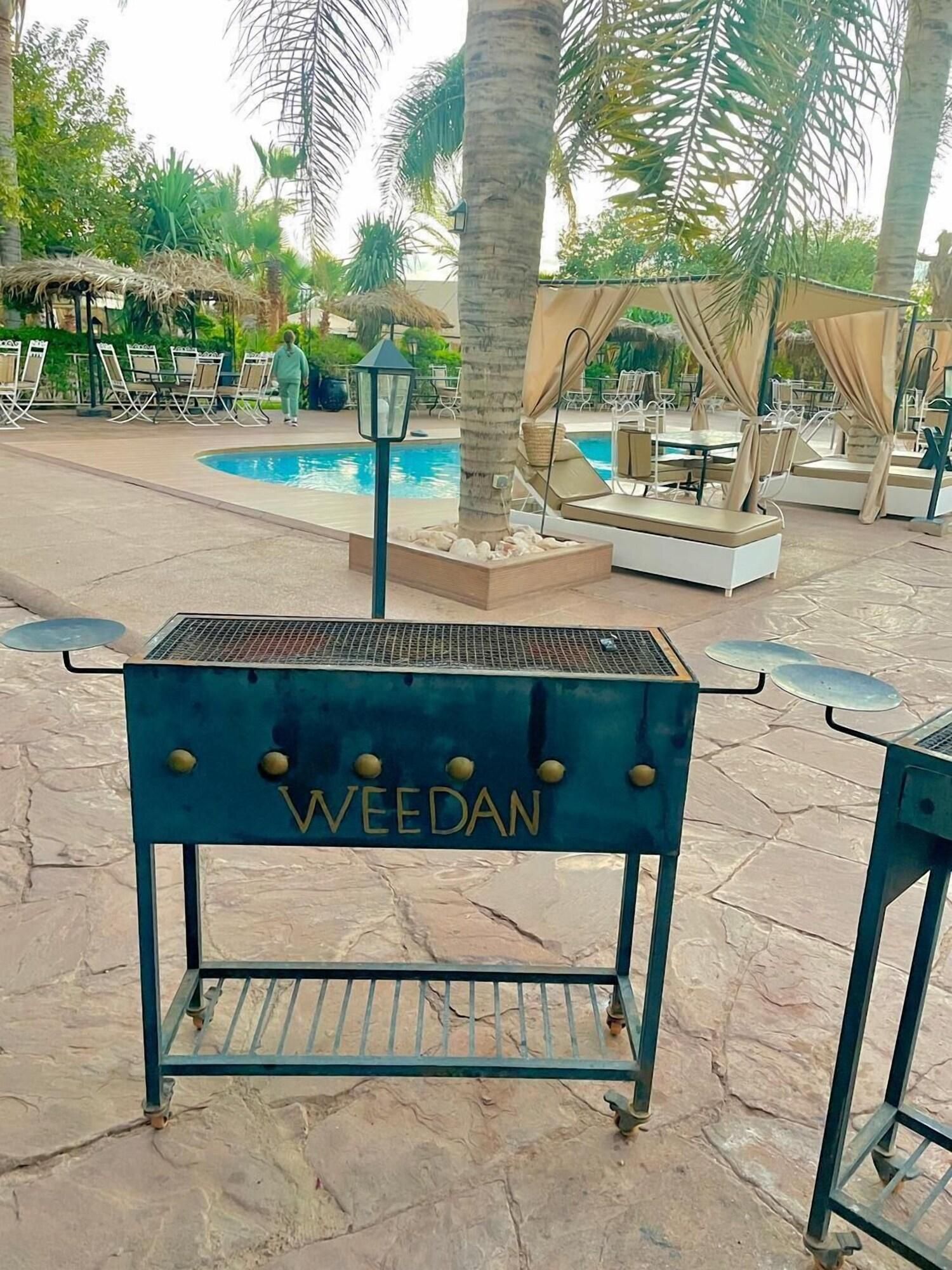 A barbecue grill with the name 'WEEDAN' in a resort setting with a pool and outdoor seating.