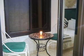 A small outdoor seating area with a table and two chairs, a lit candle, and a window with a view of a bed. - Weedan Ferme D'hôtes (Marrakech)