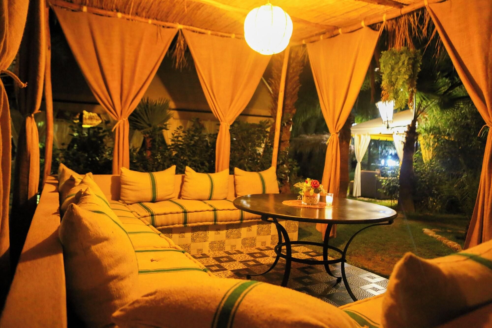 A cozy outdoor seating area with a sofa and a round table, surrounded by curtains and a hanging light fixture.
