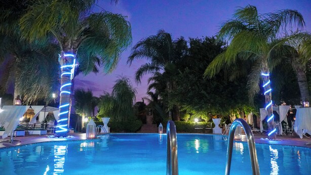 Ein Swimmingpool mit blauer Beleuchtung, Palmen und Sitzbereichen im Freien.