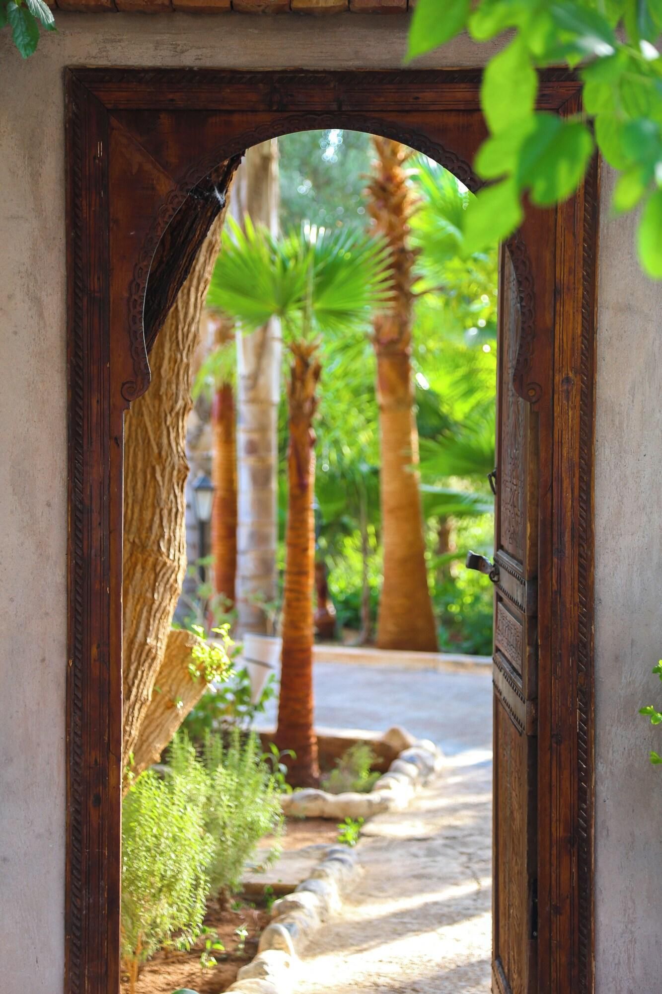 An arched wooden doorway leading to a pathway lined with palm trees and greenery.