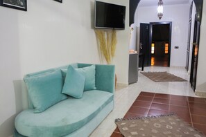 A living room with a teal sofa, a flat-screen TV, and a decorative vase with pampas grass. - Weedan Ferme D'hôtes (Marrakech)