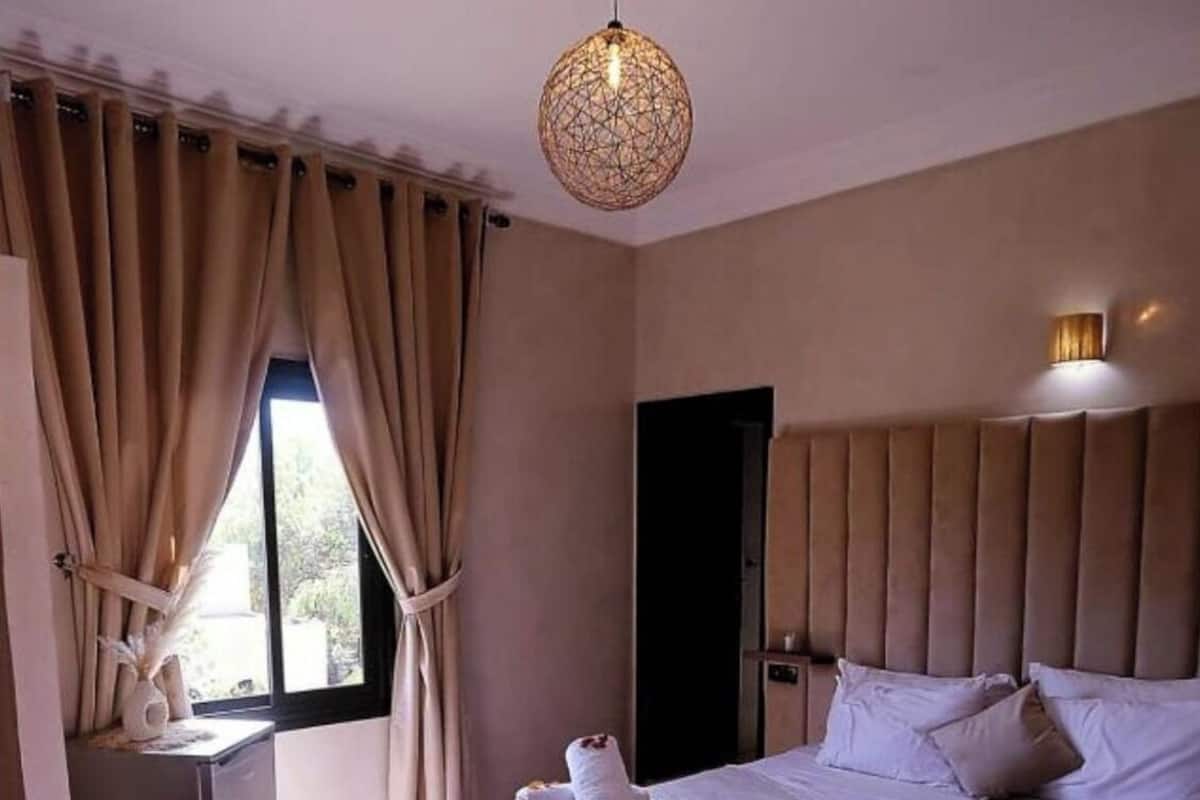 Un dormitorio con una cama grande, una mesita de noche, una ventana con cortinas y una lámpara colgante.