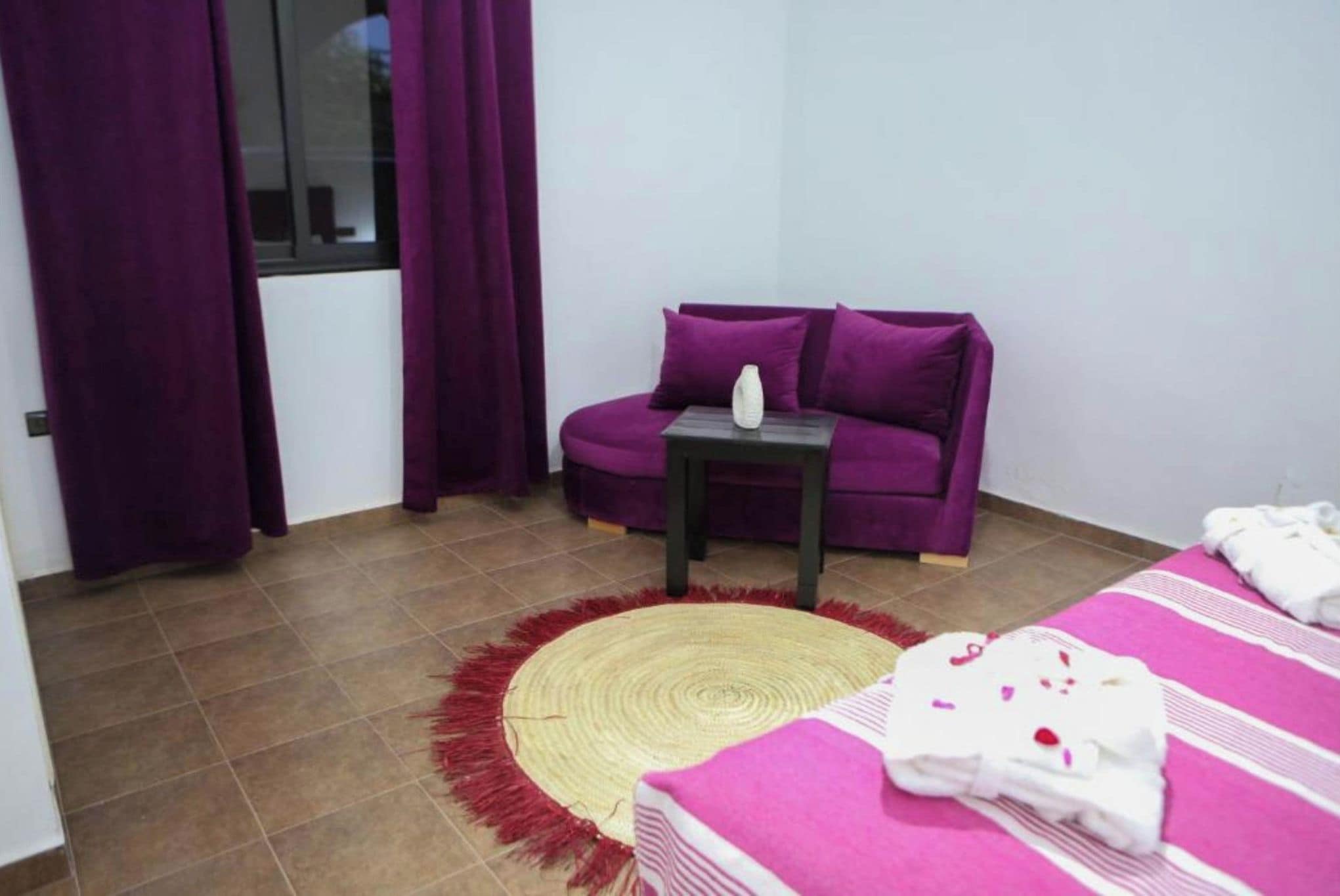 A room with a bed, a purple sofa, a small table, and a window with purple curtains.