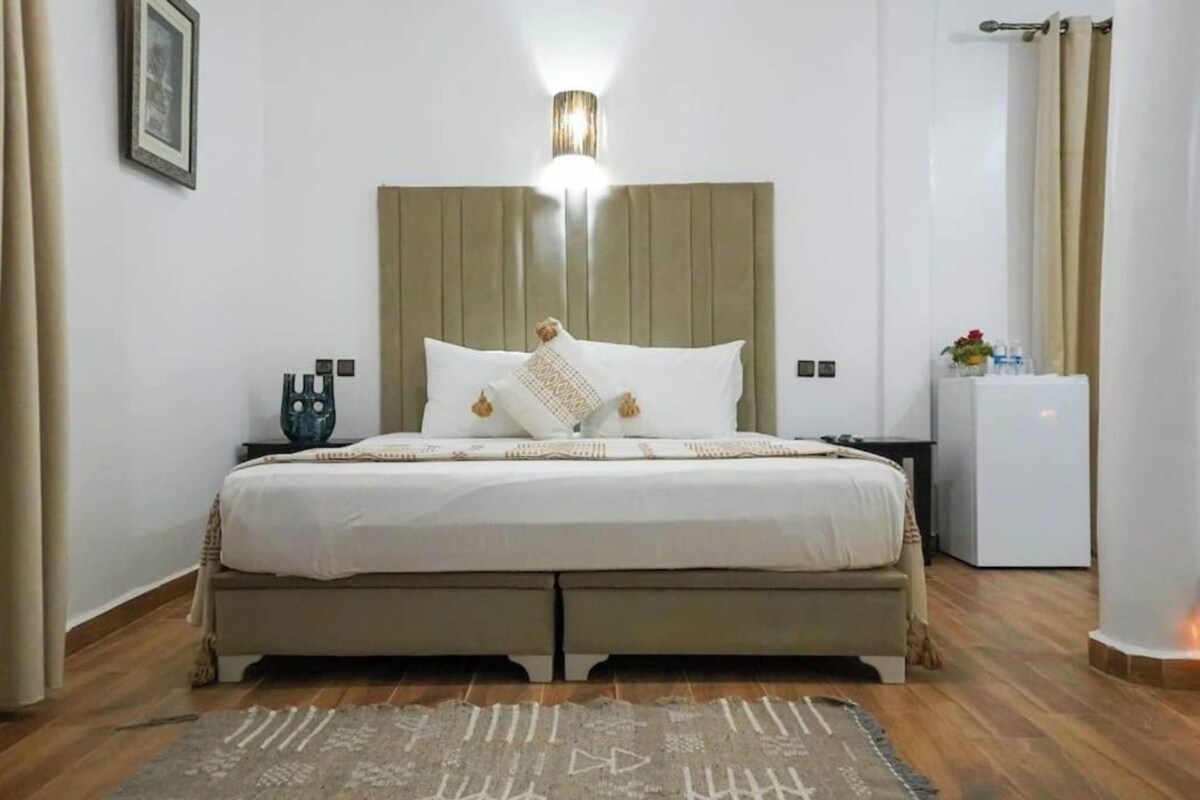 A bedroom with a bed, bedside table, nightstand, and a wall-mounted light fixture.