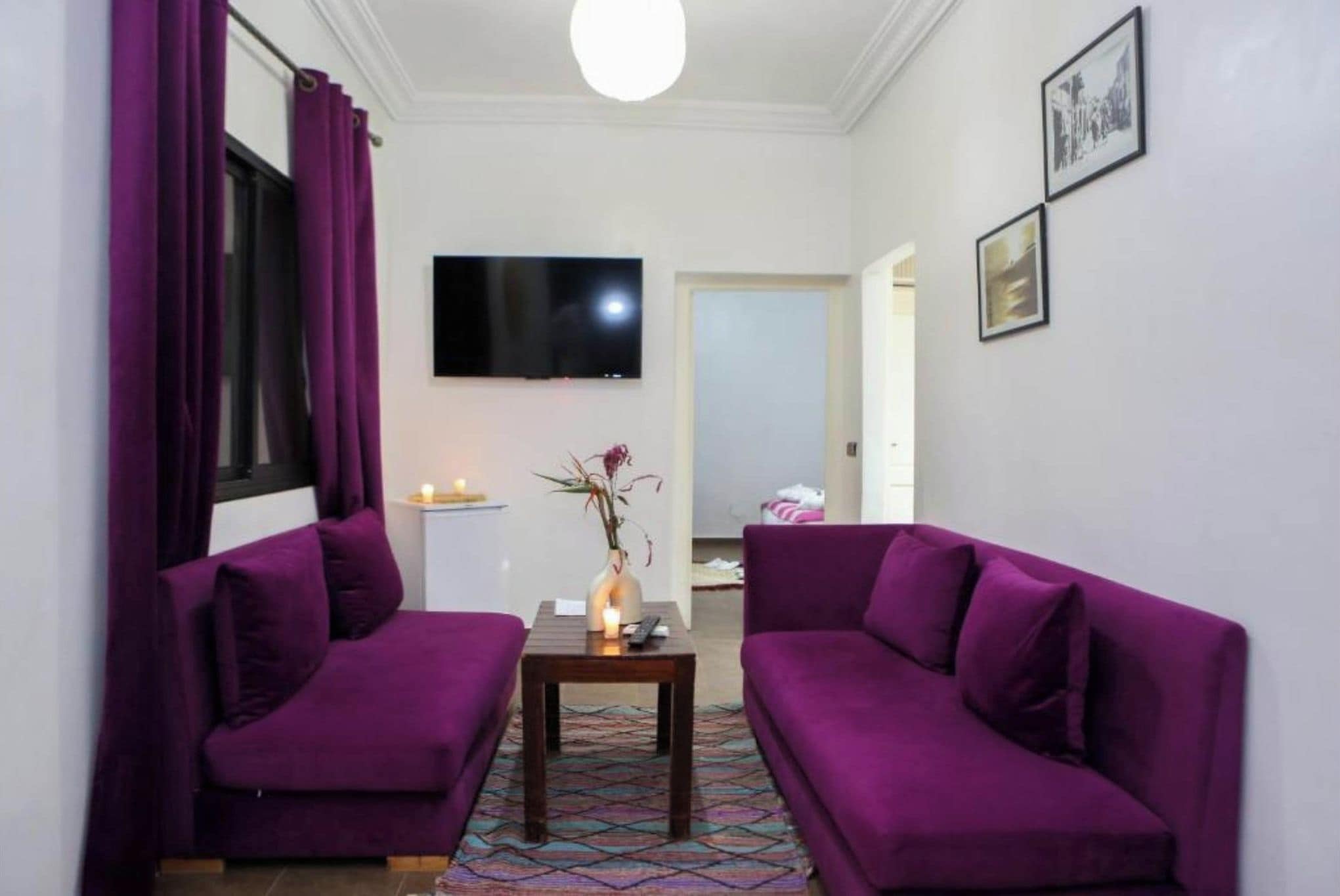A living room with two purple sofas, a small table with a candle, and a TV on the wall.