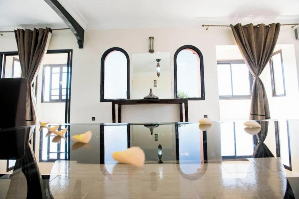 A room with a glass table, two arched windows, and a central light fixture.