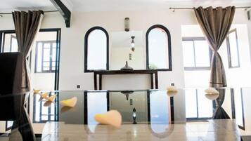 A room with a glass table, two arched windows, and a central light fixture.