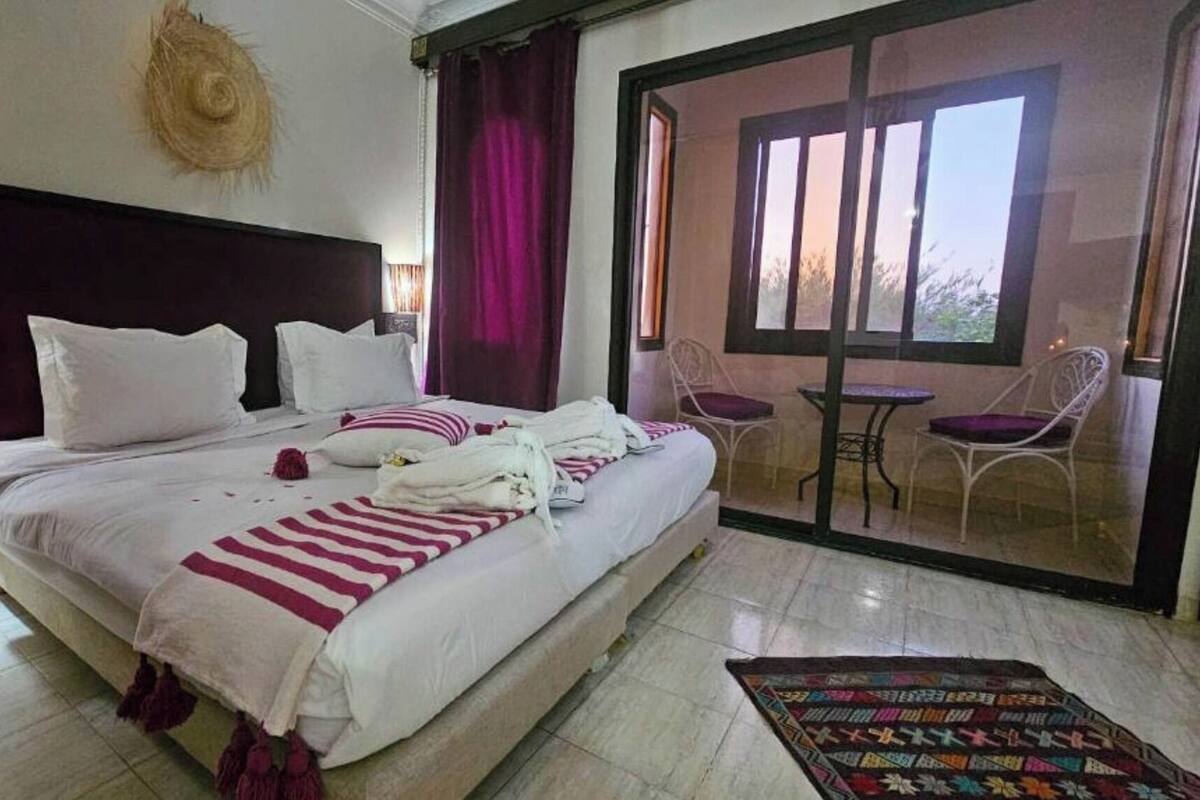 Habitación de hotel con una cama grande, cabecero, ventana con cortinas, balcón con sillas y una alfombra estampada.