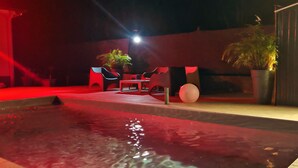 Zona de piscina exterior con iluminación roja, asientos y plantas en macetas.