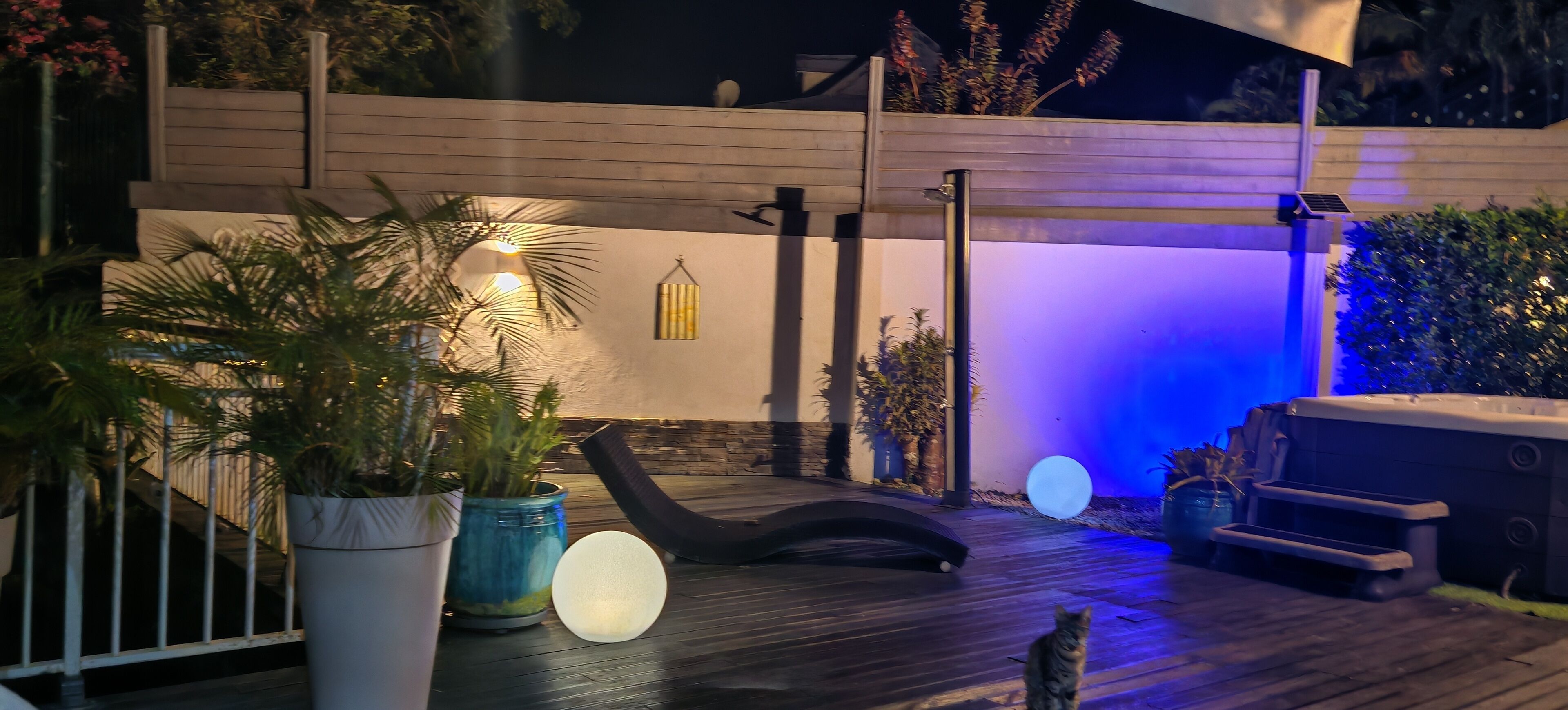 Een terras met een houten dek, een zwarte loungestoel, een jacuzzi en potplanten.