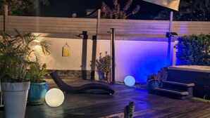 Un espacio al aire libre con terraza de madera, una silla de lounge negra, un jacuzzi y plantas en macetas.