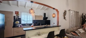 A modern kitchen with a central island, black countertops, and pendant lighting. There is a dining area with a sofa and chairs.