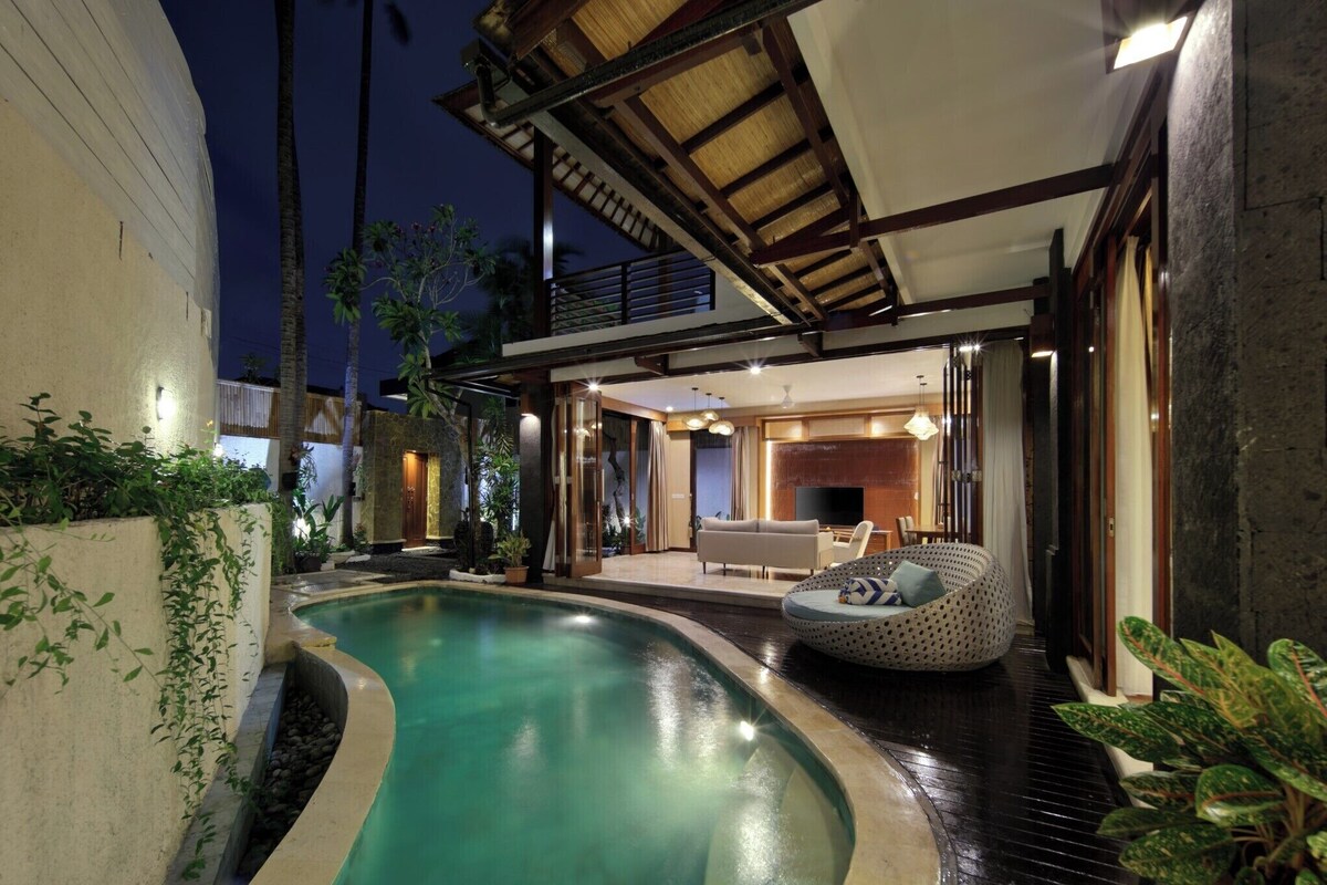 Ein moderner Poolbereich im Freien mit gewölbtem Design, überdachtem Sitzbereich und gut beleuchtetem Innenraum.
