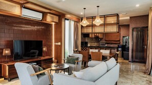 Ein modernes Wohnzimmer mit Flachbildfernseher, einer Couch, Sesseln und einem Essbereich mit Tisch und Stühlen.