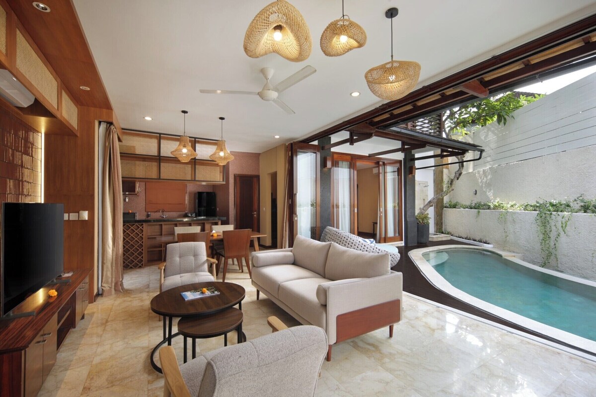 Ein modernes Wohnzimmer mit Sofa, Couchtisch und Fernseher, ein Küchenbereich und ein Pool.