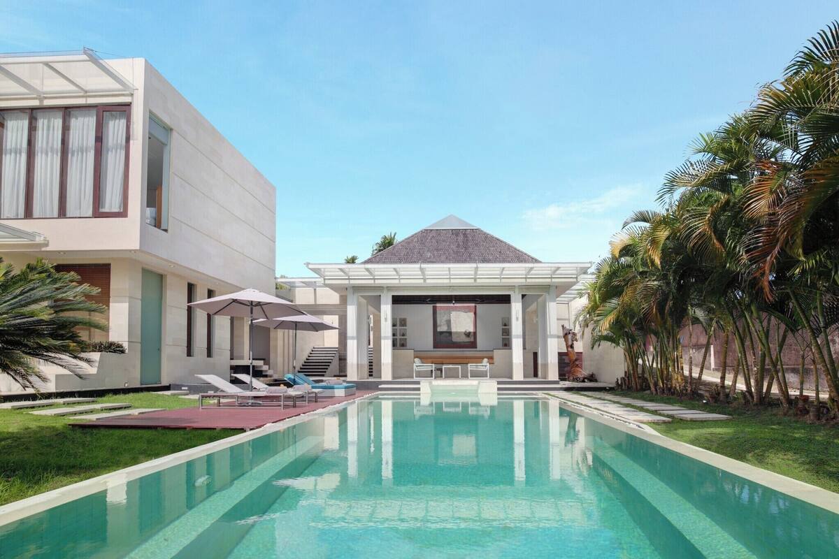 Un área de piscina moderna con una piscina cristalina, sillas de descanso y sombrillas.