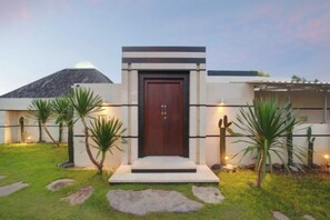A modern building with a prominent entrance, a sloped roof, and a well-maintained lawn with rocks and plants. - Nara Villa Canggu By Ini Vie Hospitality (Payangan)