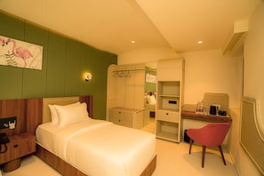 A hotel room with a bed, a desk with a chair, a wardrobe, and a painting on the wall. - Hotel Harriet (Rameshwaram)