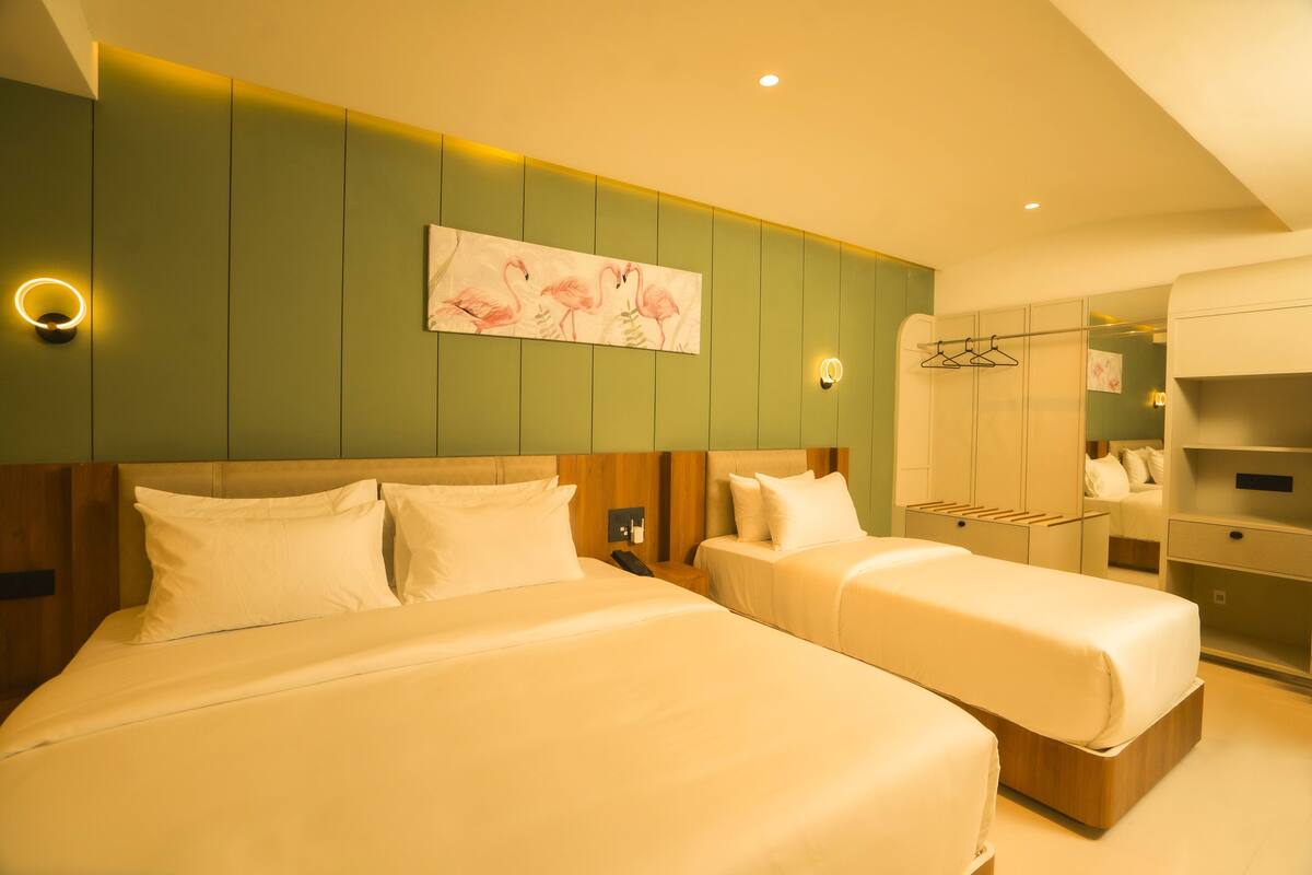 A hotel room with two beds, a green accent wall, and a painting of flamingos.