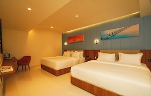 A hotel room with two beds, a desk with a chair, a painting on the wall, and a view of a bridge. - Hotel Harriet (Rameshwaram)