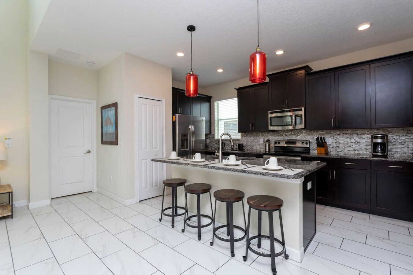 A modern kitchen with dark cabinets, stainless steel appliances, a central island with stools, and pendant lighting.