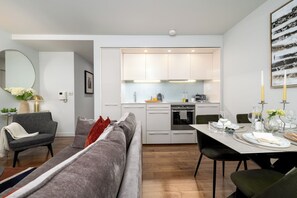 A modern kitchen with white cabinets, a built-in oven, and a dining area with a table set for two. - Liverpool Street - Your Apartment (London)