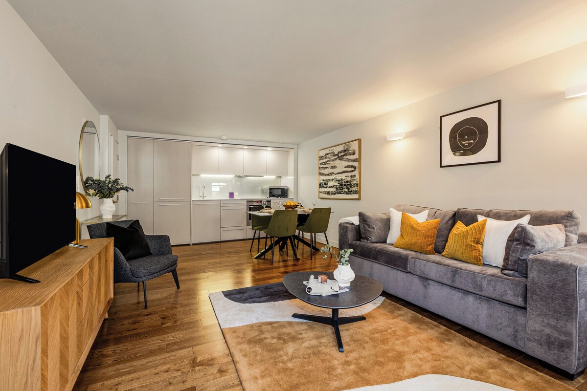 A modern living room with a grey sofa, a wooden TV stand, and a dining area with a table and chairs.
