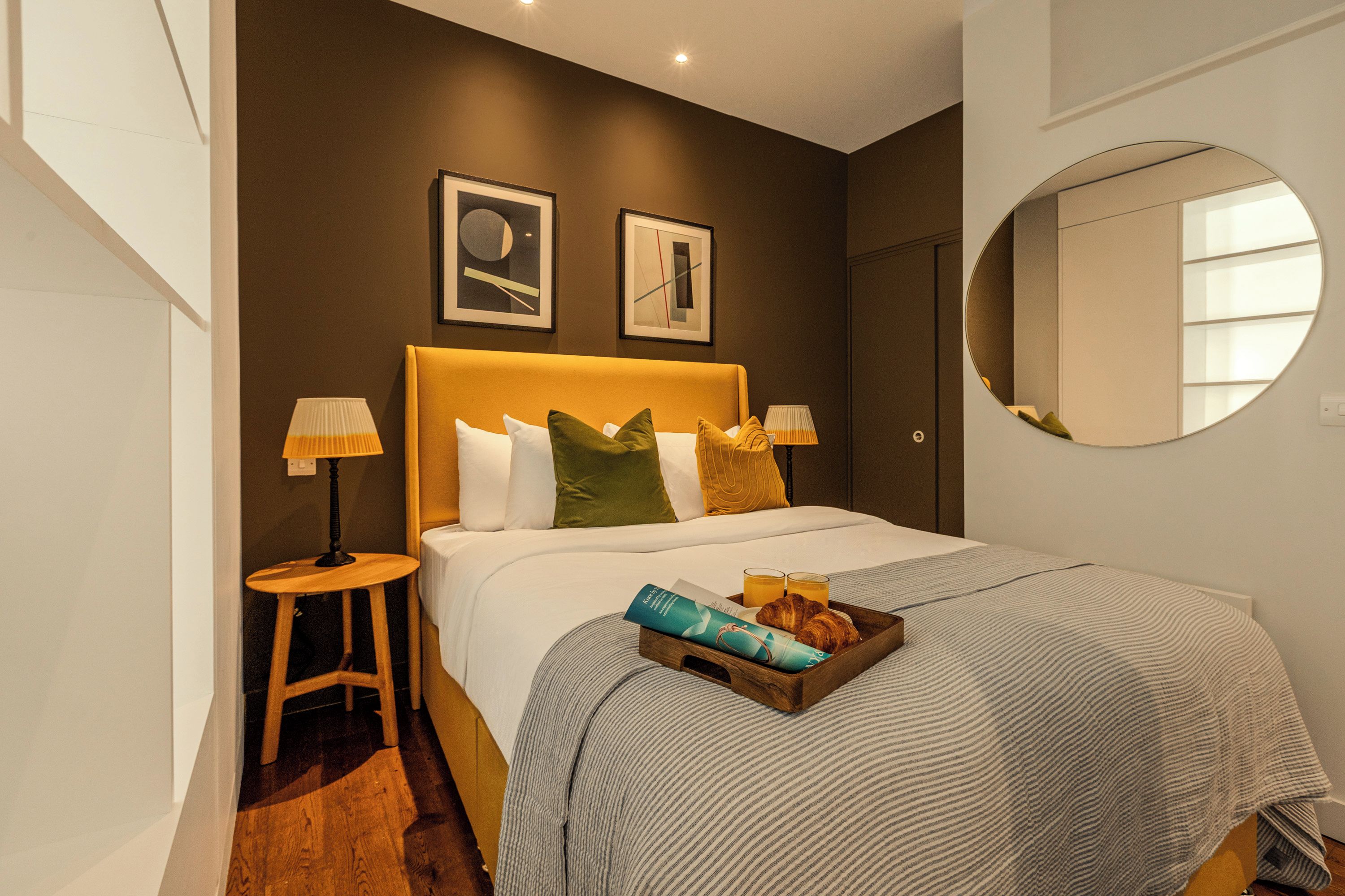 A neatly made bed with a striped bedspread, two pillows, and a bedside table with a lamp.
