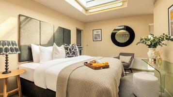 A modern hotel room with a large bed, a glass coffee table, a round mirror, and a small round ottoman.