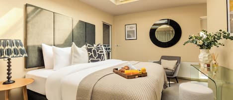 Ein modernes Hotelzimmer mit einem großen Bett, einem Glastisch, einem runden Spiegel und einem kleinen, runden Hocker.