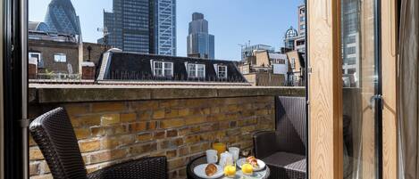 A rooftop terrace with wicker furniture, a brick wall, and a table set for breakfast.