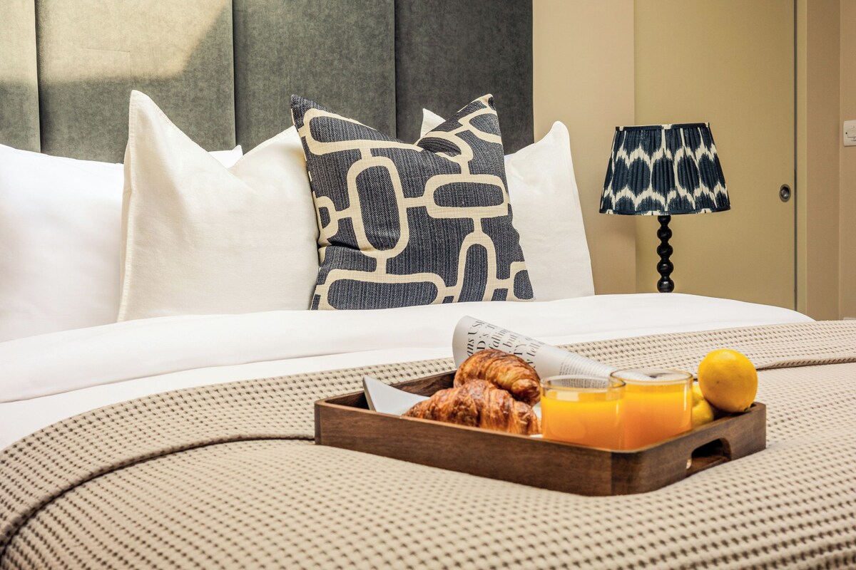 A neatly made bed with white linens, a tray of croissants, orange juice, and a lemon.