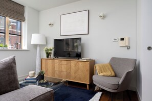 A modern living room with a television on a wooden cabinet, a comfortable armchair, and a glass coffee table. - Liverpool Street - Your Apartment (London)