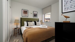 A bedroom with a bed, bedside tables, a lamp, a picture frame, and a window. - Liverpool Street - Your Apartment (London)