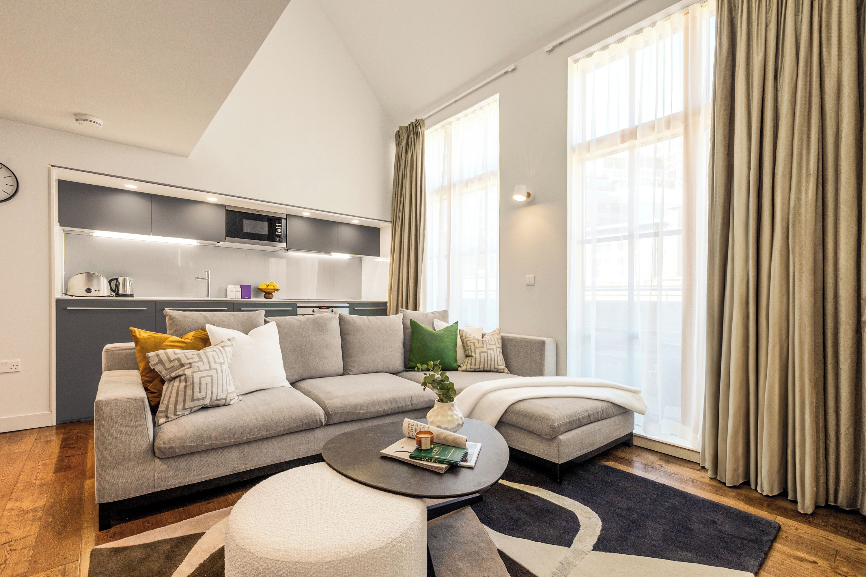 A modern living room with a grey sofa, a coffee table, and a kitchen in the background.
