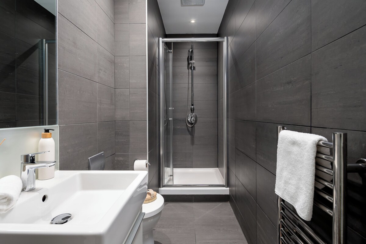 A modern bathroom with a glass-enclosed shower, a white sink, and a towel rack.