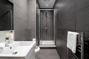 A modern bathroom with a glass-enclosed shower, a white sink, and a towel rack. - Liverpool Street - Your Apartment (London)