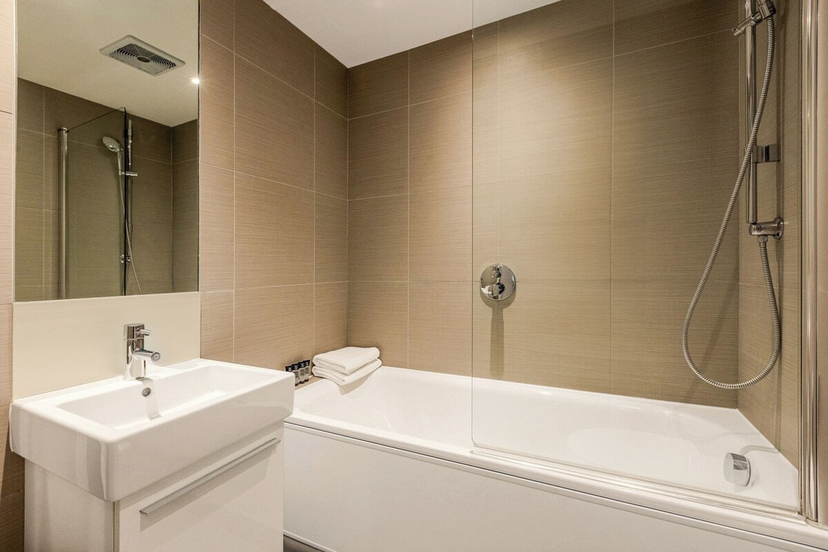 A modern bathroom with a white sink, a glass-enclosed shower, and beige tiled walls.