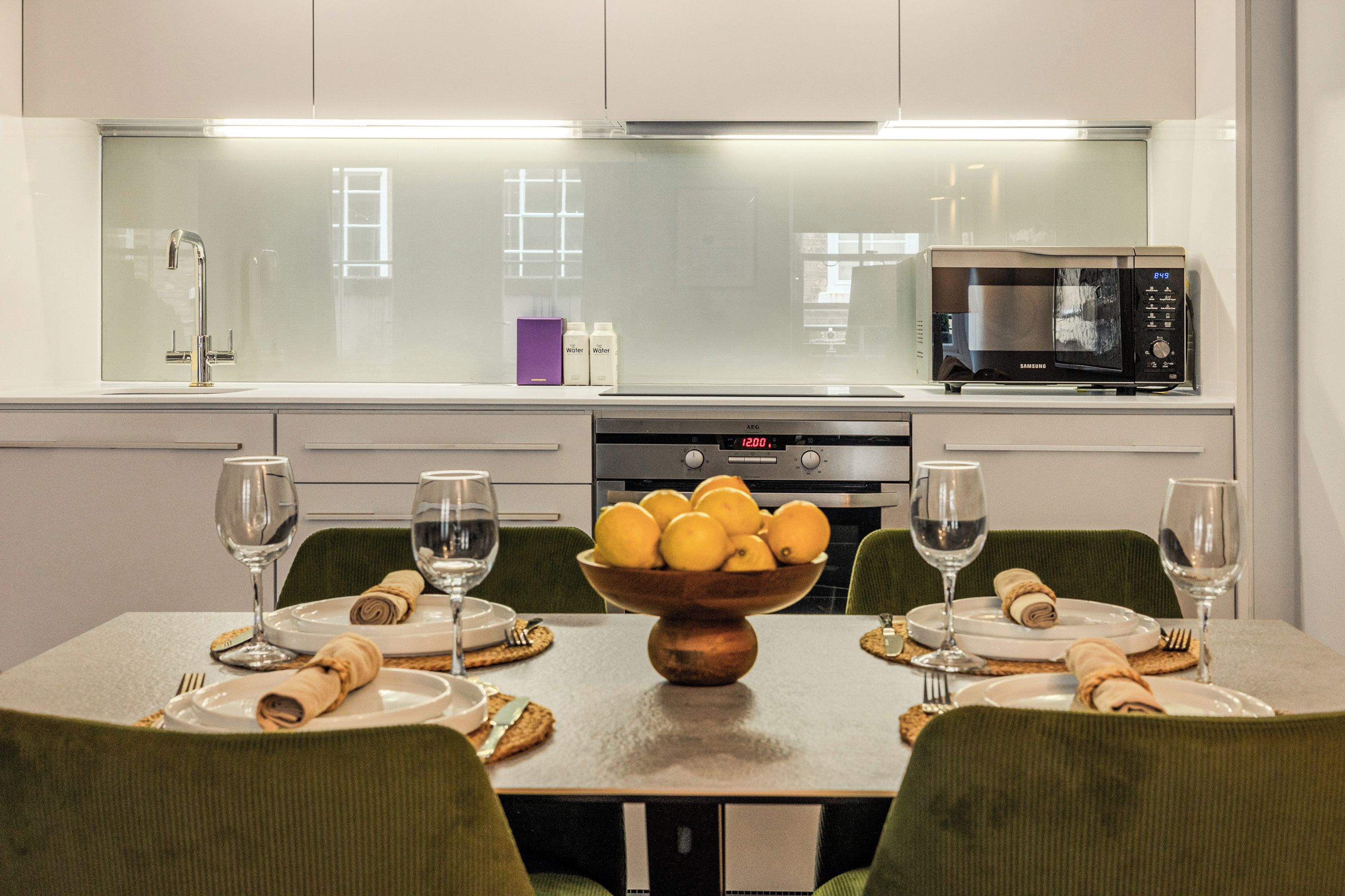 Una cocina moderna con microondas, un reloj digital y un cuenco de limones en la encimera.