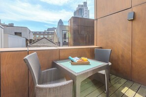 A balcony with wicker chairs and a table, a tray with croissants and orange juice, and a cityscape view. - Liverpool Street - Your Apartment (London)